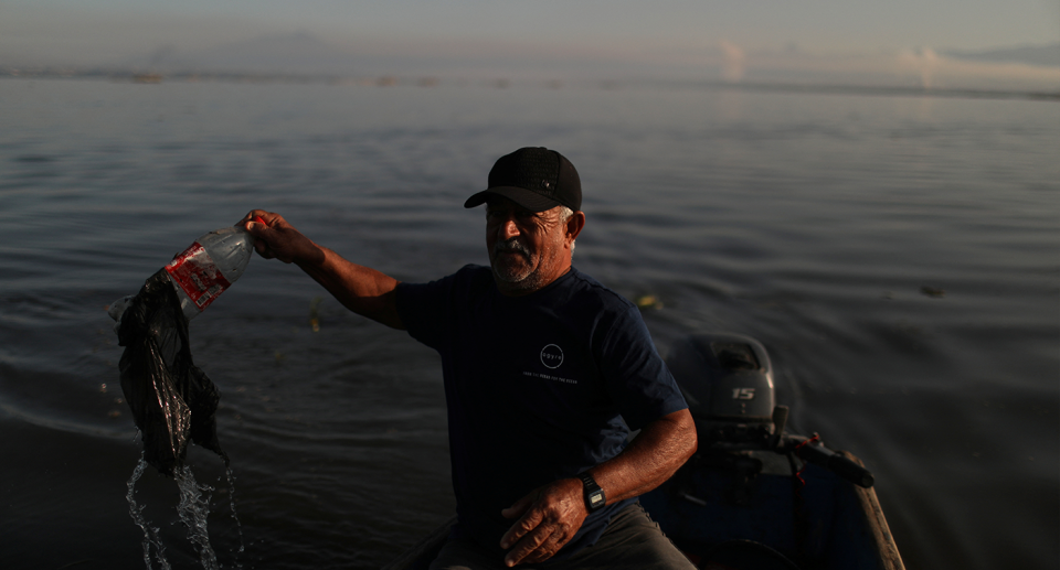 Ailton Rodrigues stands in a boat and holds up a bottle