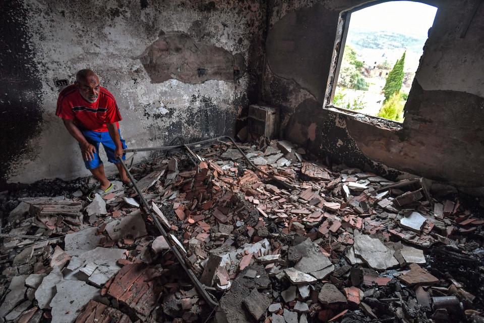 A man picks up a damaged metal frame while going through the rubble of a destroyed building in the aftermath of a forest fire near the town of Melloula in northwestern Tunisia close to the border with Algeria on July 26, 2023. At least 300 people were evacuated by sea and by land from Melloula, according to the Tunisian national guard, as fires raged again there on July 24. A severe heatwave has been reflected across much of southern Europe and northern Africa, killing dozens and forced mass evacuations. (Photo by FETHI BELAID / AFP) (Photo by FETHI BELAID/AFP via Getty Images)