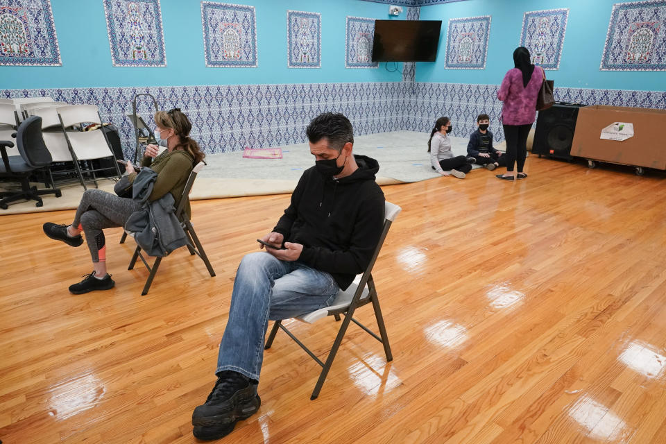 Mosque member Albert Capa's, foreground, wife and children are seen in the background as he sits in the observation area after being inoculated with the Johnson & Johnson COVID-19 vaccine at a pop up vaccinations site the Albanian Islamic Cultural Center, Thursday, April 8, 2021, in the Staten Island borough of New York. Ahead of Ramadan, Islamic leaders are using social media, virtual town halls and face-to-face discussions to spread the word that it’s acceptable for Muslims to be vaccinated during daily fasting that happens during the holy month. (AP Photo/Mary Altaffer)