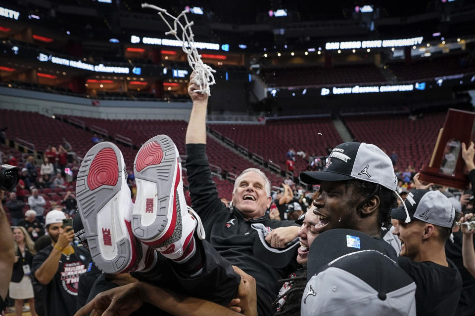 San Diego State head coach Brian Dutcher holds the remains of the net and is hoisted in the air by his team after a Elite 8 college basketball game between Creighton and San Diego State in the South Regional of the NCAA Tournament, Sunday, March 26, 2023, in Louisville, Ky. San Diego State won 57-56. (AP Photo/Mike Stewart)