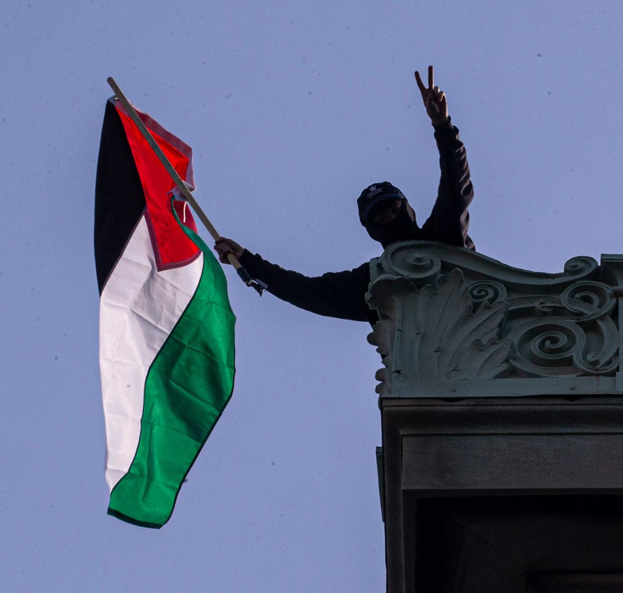 One of the protesters who took over Hamilton Hall at Columbia University waves a Palestinian flag from the roof of the building April 30, 2024, as hundreds of protesters cheered from the street below.