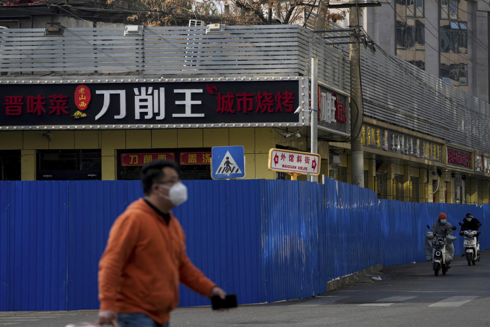 A man wearing a face mask and motorists pass by metal barriers set up around the shuttered shop houses that were locked down as part of COVID-19 controls in Beijing on Thursday, Nov. 10, 2022. China's capital Beijing has closed city parks and imposed other restrictions as the country faces a new wave of COVID-19 cases. (AP Photo/Andy Wong)