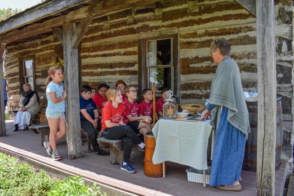 Volunteer Sharon Sprague, right, teaches students from R.C. Waters Elementary School and St. Boniface Catholic School how to make butter on the porch of the Oak Harbor Log Cabin.