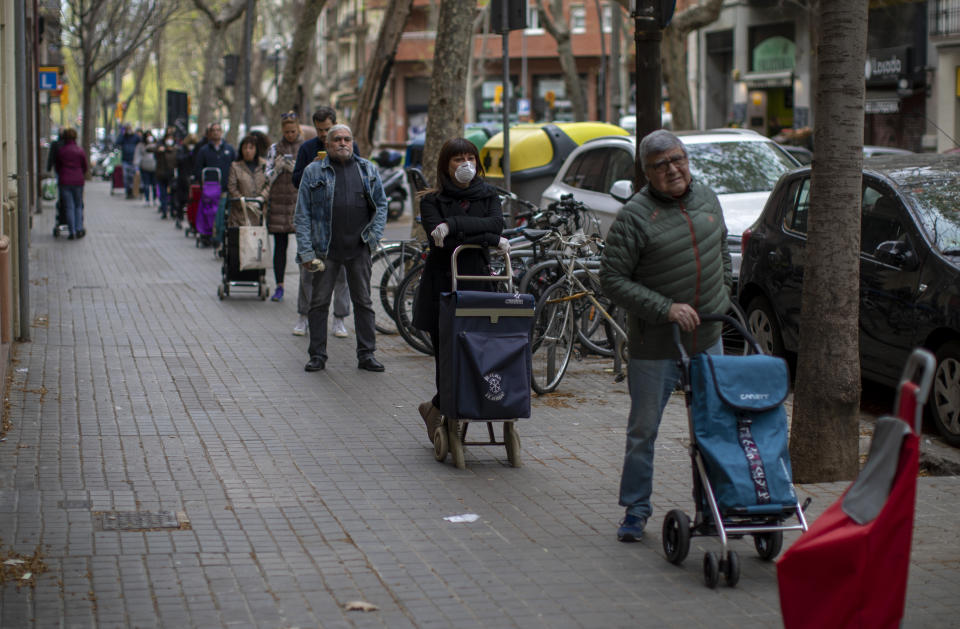 People line up to buy supplies from a shop during the coronavirus outbreak in Barcelona, Spain, Friday, March 27, 2020. The new coronavirus causes mild or moderate symptoms for most people, but for some, especially older adults and people with existing health problems, it can cause more severe illness or death. (AP Photo/Emilio Morenatti)