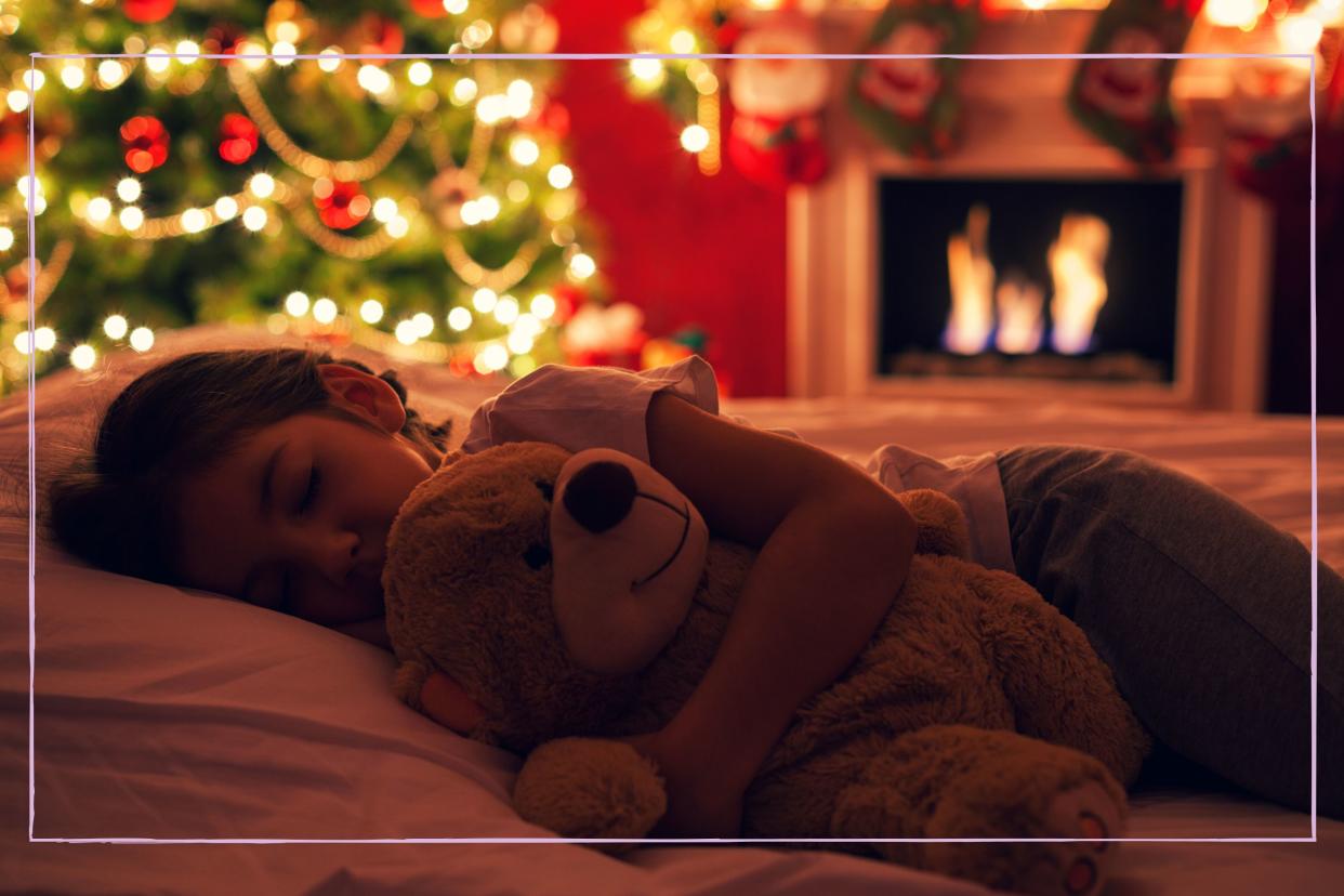  A young girl asleep in front of a Christmas tree. 