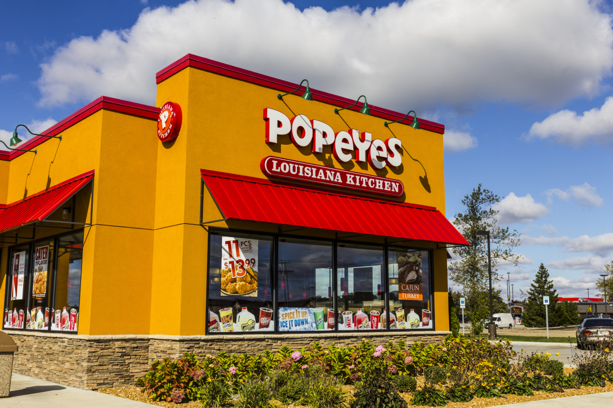 Front exterior of Popeyes Louisiana Kitchen fast food restaurant, Anderson, Indiana with a front garden and the parking lot to the left, on a sunny day in summer