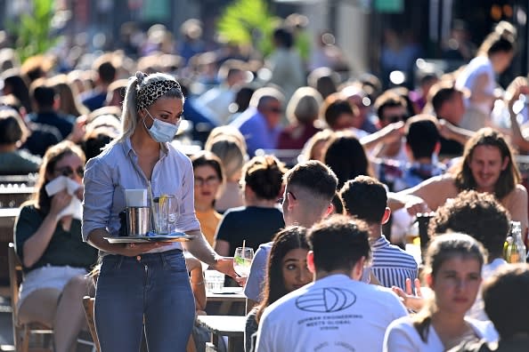 A waitress wearing a protective face covering brings drinks to customers in the late summer sunshine at outside tables in Soho, central London.