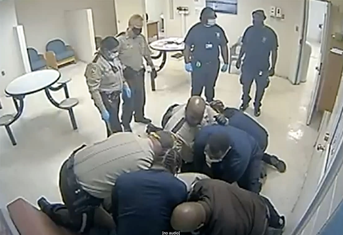 As four officers and orderlies in mask stand by, about five people subdue Irvo Otieno, who is not visible and is lying on the hospital floor.