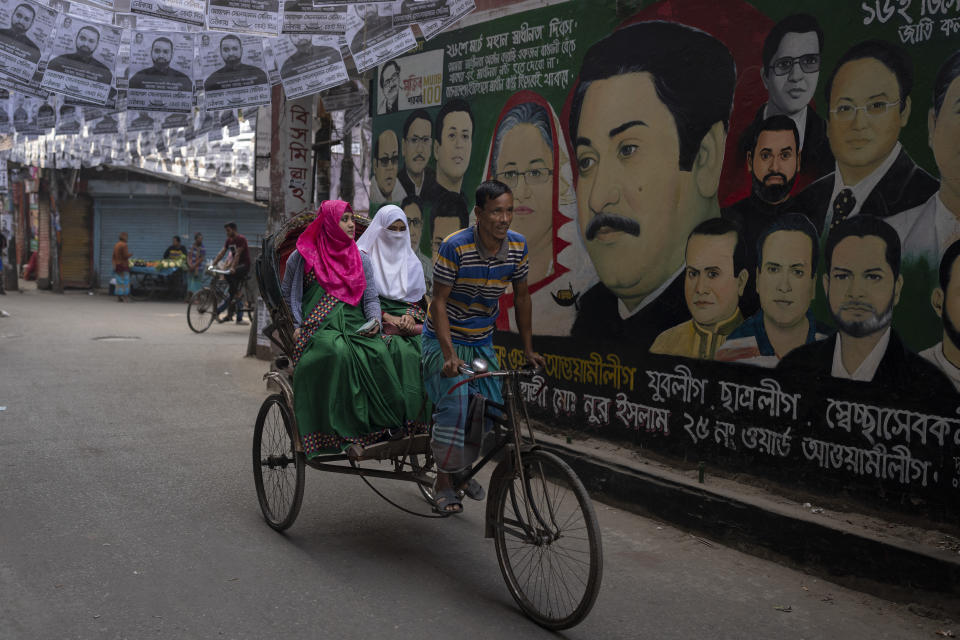 A rickshaw ferrying passengers rides past a mural displaying portraits of Bangladesh Prime Minister Sheikh Hasina, her father and founder of the nation Sheikh Mujibur Rahman and other leaders in Dhaka, Bangladesh, Friday, Jan. 5, 2024. (AP Photo/Altaf Qadri)