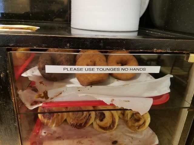 A display case with donuts and a sign that reads "PLEASE USE TOuNGES NO HANDS," indicating a misspelling of "tongs."