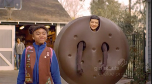 Girl Scout smiling proudly next to a man dressed as a cookie