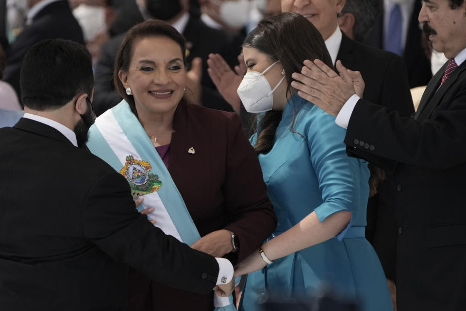 President Xiomara Castro smiles as she receives the presidential sash, and her husband former President Manuel Zelaya who was ousted by a military coup in 2009, right, applauds during her inauguration as the first female president in Tegucigalpa, Honduras, Thursday, Jan. 27, 2022. (AP Photo/Moises Castillo)