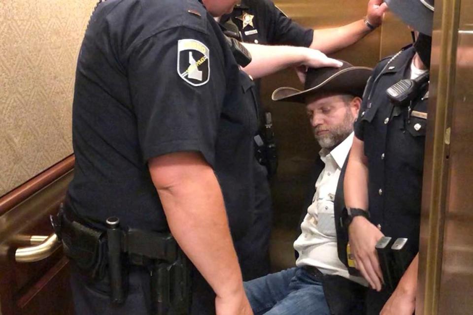In 2020, Ammon Bundy, rear, was wheeled into an elevator in a chair following his arrest at the Idaho Statehouse in Boise. In 2023, he rolled out of Idaho fleeing legal woes.