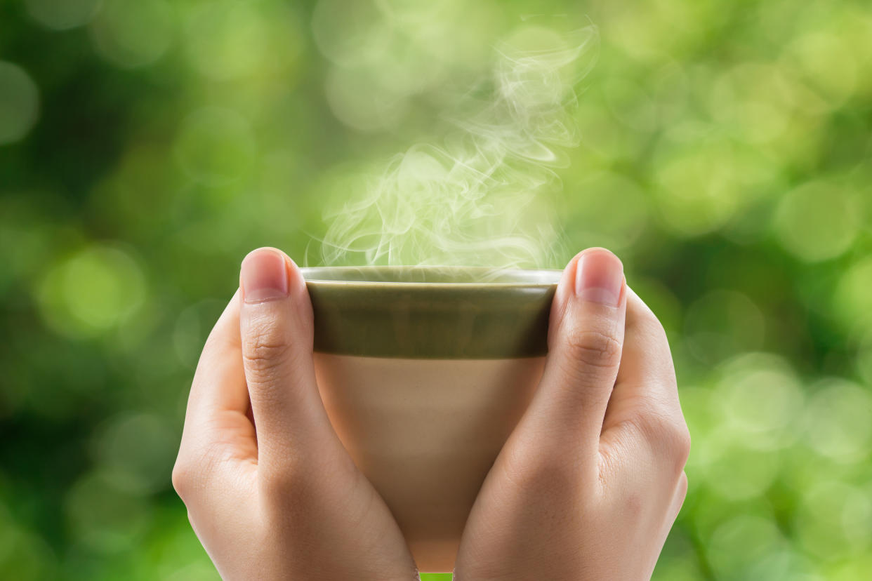 Hands holding a mug of green tea.