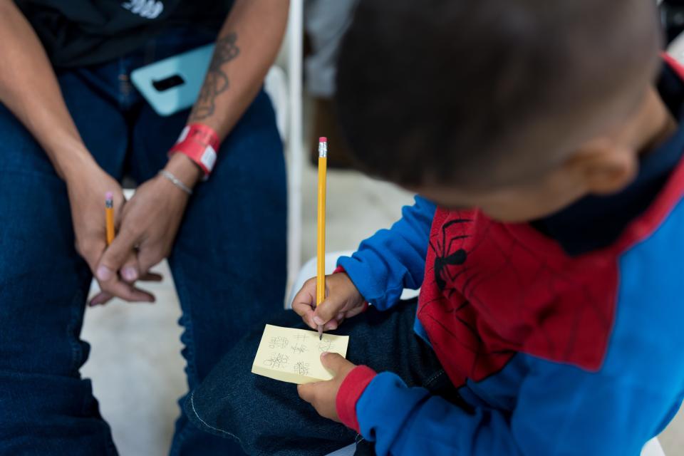 Migrants play tic-tac-toe at the city of El Paso's Migrant Welcome Center in Northeast El Paso while they wait for a bus to take them to their final destination.
