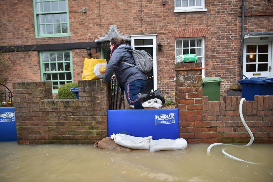 A woman carrying shopping bags through flood water, as pumps and flood barriers help to keep the water from flooding homes in Gloucester Road in Tewkesbury, Gloucestershire, following the aftermath of Storm Dennis.