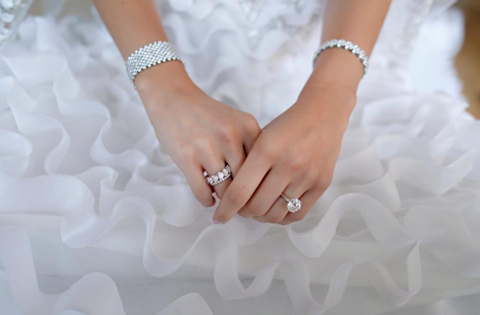 A bride places her hands on a ruffled wedding dress to show off their ring.