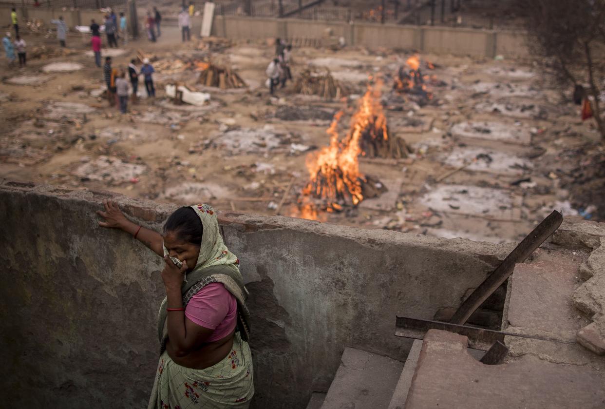 A woman covers her nose as smoke and fumes rise from the burning funeral pyres of the patients who died of COVID-19 from her house near a makeshift crematorium on May 9, 2021, in New Delhi, India. India broke a fresh record on Thursday with over 412,000 new cases of coronavirus as the total number of those infected according to Health Ministry data neared 20 million. The real figure could be up to ten times higher, many health experts say, due to a lack of widespread testing or reporting, and only patients who succumbed in hospitals being counted. Hospitals have begun turning away people suffering from COVID-19, having run out of space for the crushing number of people seeking help.