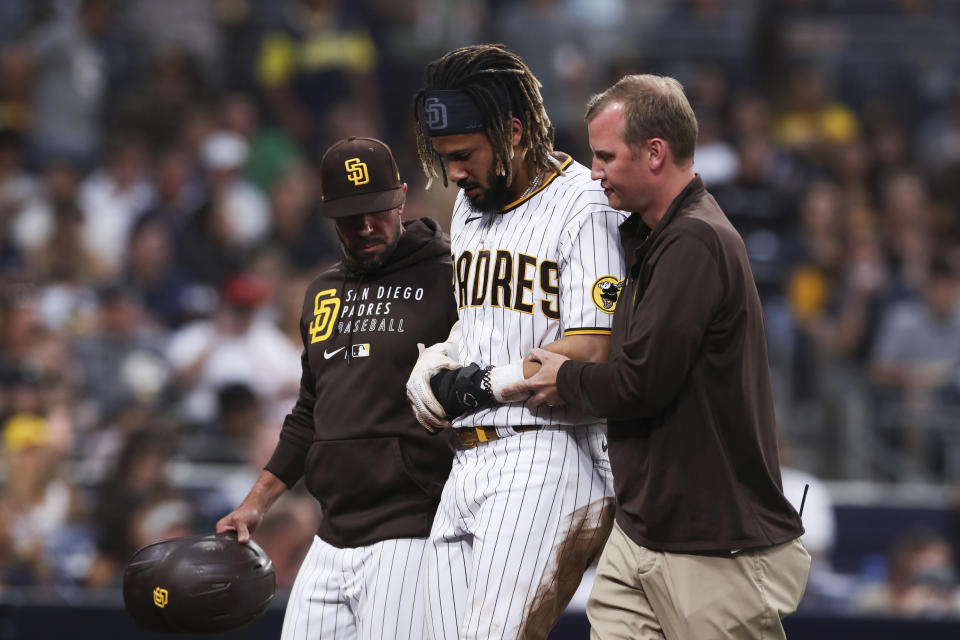 San Diego Padres' Fernando Tatis Jr., center, is helped off the field by manager Jayce Tingler, left, and a trainer during the first inning of the team's baseball game against the Colorado Rockies, Friday, July 30, 2021, in San Diego. (AP Photo/Derrick Tuskan)