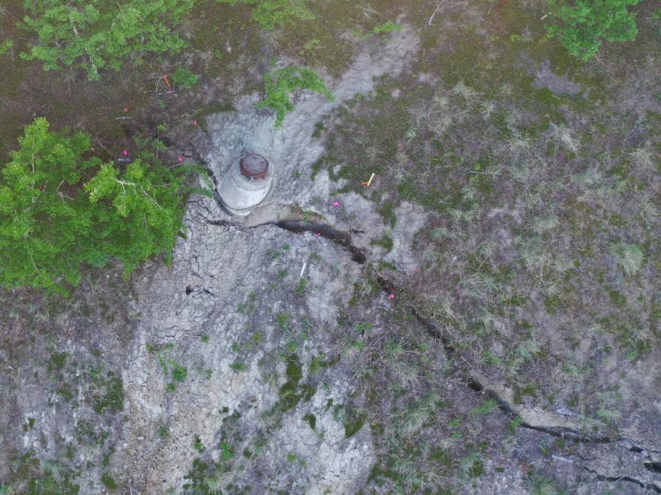 A photo taken from a drone in June 2022 shows a manhole near a large tension crack on Whitehorse's escarpment. City officials say the crack is expected to eventually cause a slide, and that threatens one of the city's main sewer lines. (City of Whitehorse - image credit)