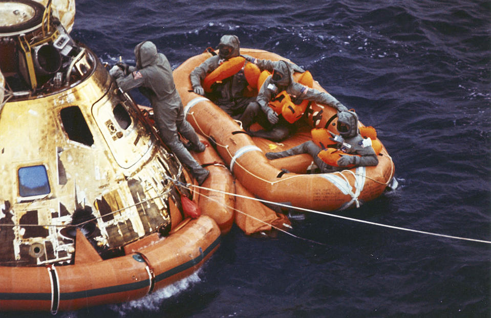 FILE - In this July 24, 1969, file photo from the U.S. Navy, Lt. Clancy Hatleberg closes the Apollo 11 spacecraft hatch as astronauts Neil Armstrong, Michael Collins, and Buzz Aldrin, Jr., await helicopter pickup from their life raft after splashdown in the Pacific Ocean, 900 miles southwest of Hawaii, returning to Earth from a successful lunar landing mission. Hatleberg's mission was to decontaminate the astronauts and their command module, Columbia, immediately following splashdown. The astronauts' trip to the moon concluded with a stay in Hawaii. July 20 marked the 50th anniversary of the moon landing, but after those historic first steps NASA still had to get the three astronauts safely back to Earth - and the waters off Hawaii are where the cone-shaped spacecraft splashed down. (Milt Putnam/U.S. Navy via AP, File)