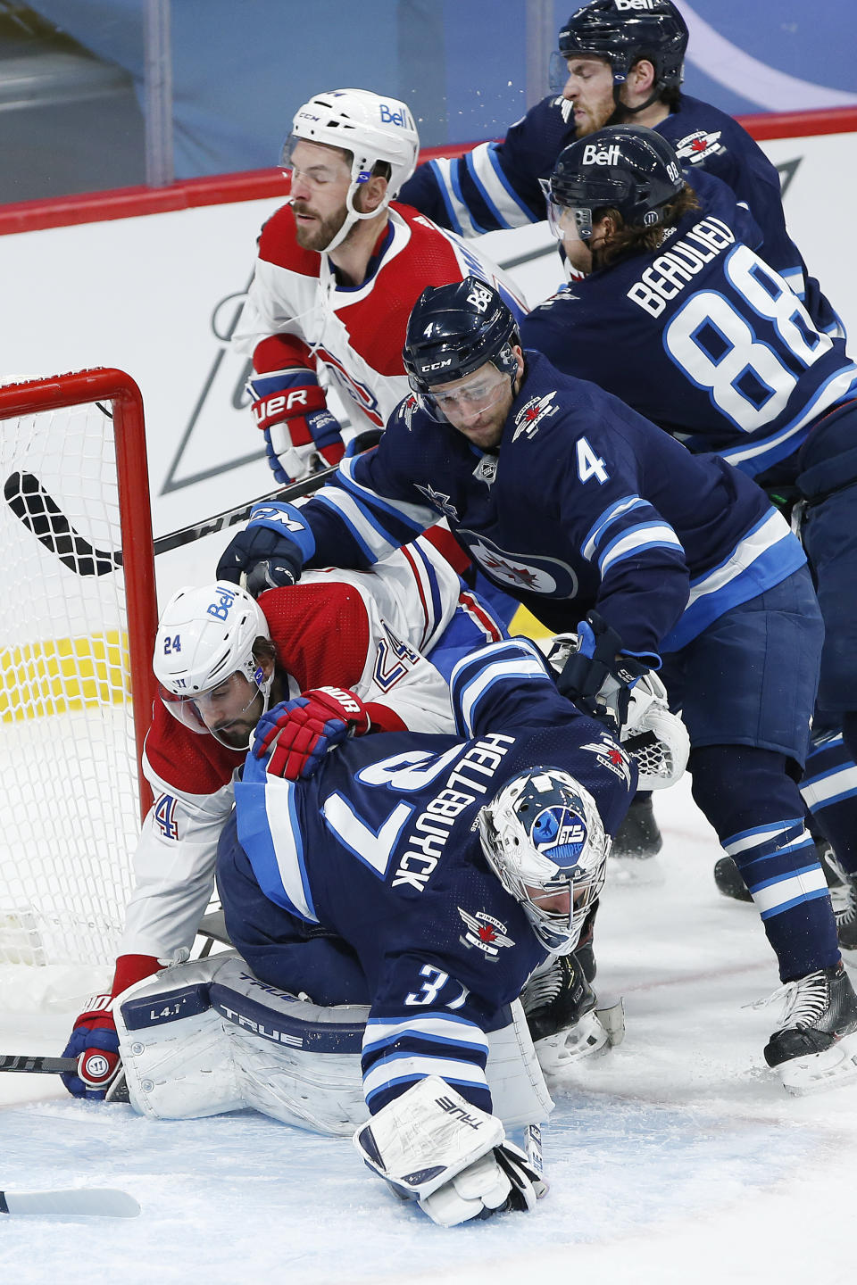 Winnipeg Jets goaltender Connor Hellebuyck (37) dives onto the rebound as Montreal Canadiens' Phillip Danault (24) crashes into him and Jets' Neal Pionk (4) defends during the second period of an NHL hockey game Saturday, Feb. 27, 2021, in Winnipeg, Manitoba. (John Woods/The Canadian Press via AP)