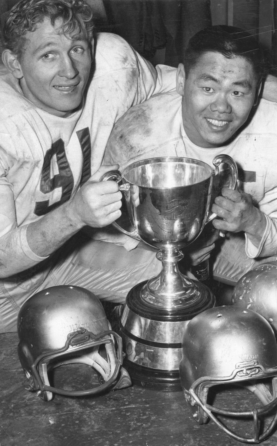 Edmonton Eskimos greats Jackie Parker, left, and Normie Kwong hold the Grey Cup after a convincing victory over the Montreal Alouettes at Varsity Stadium in Toronto in 1956. (The Globe and Mail/The Canadian Press)