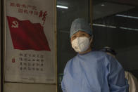 A health worker looks out near a poster with the Chinese communist party flag and the slogan "Follow the Communist Party, Fulfill the China Dream" at a health station near a sealed off neighborhood in Wuhan in central China's Hubei province on Friday, April 3, 2020. Sidewalk vendors wearing face masks and gloves sold pork, tomatoes, carrots and other vegetables to shoppers Friday in the Chinese city where the coronavirus pandemic began as workers prepared for a national memorial this weekend for health workers and others who died in the outbreak. (AP Photo/Ng Han Guan)