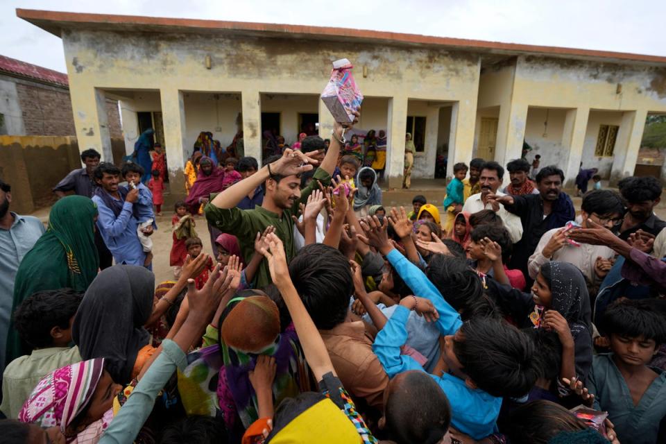 A volunteer distributes food items among children at a camp set up in a school building for internally displaced people from coastal areas, as Cyclone Biparjoy was approaching, in Badin, Pakistan's southern district in the Sindh province (AP)