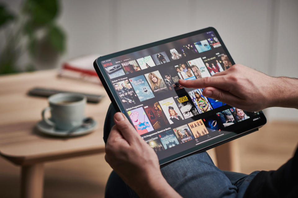A mans hand scrolling through Netflix on an Apple iPad Pro