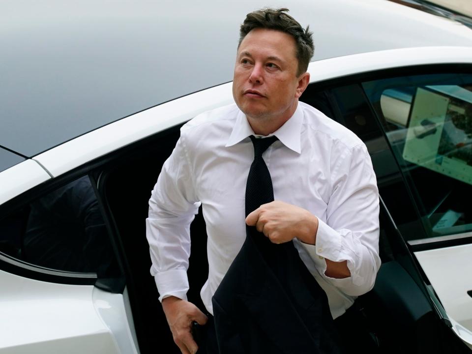 Tesla CEO Elon Musk in a white shirt and tie exits the backseat of a white Tesla