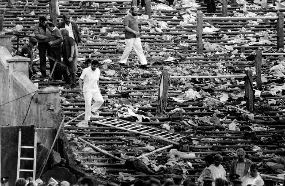 FILE - In this May 29, 1985 file photo, spectators walk through the personal belongings of victims littering the stands, after a clash between rival soccer fans at the European Cup Final at Heysel Stadium in Brussels. Friday, May 29, 2020 marks 35 years since 39 victims lost their lives during a European Cup football match between Liverpool and Juventus due to a surge of rival supporters resulting in a collapsed wall. (AP Photo, File)