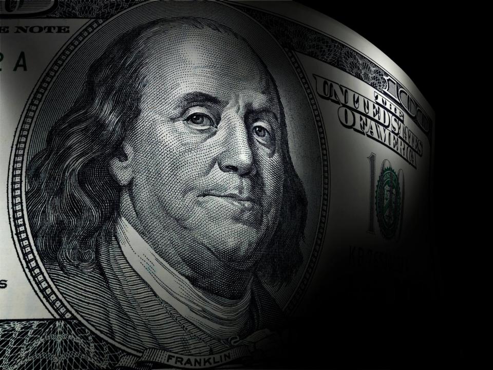 A close-up of Ben Franklin's portrait on a one hundred dollar bill, set against a dark background.