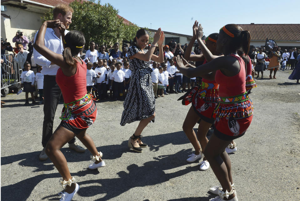 Britain's royal couple Prince Harry and Meghan Duchess of Sussex, move with dancers on their arrival at the Nyanga Methodist Church in Cape Town, South Africa, Monday, Sept, 23, 2019, which houses a project where children are taught about their rights, self-awareness and safety, and are provided self-defence classes and female empowerment training to young girls in the community. The royal couple are starting their first official tour as a family with their infant son, Archie (Courtney Africa / Africa News Agency via AP, Pool)