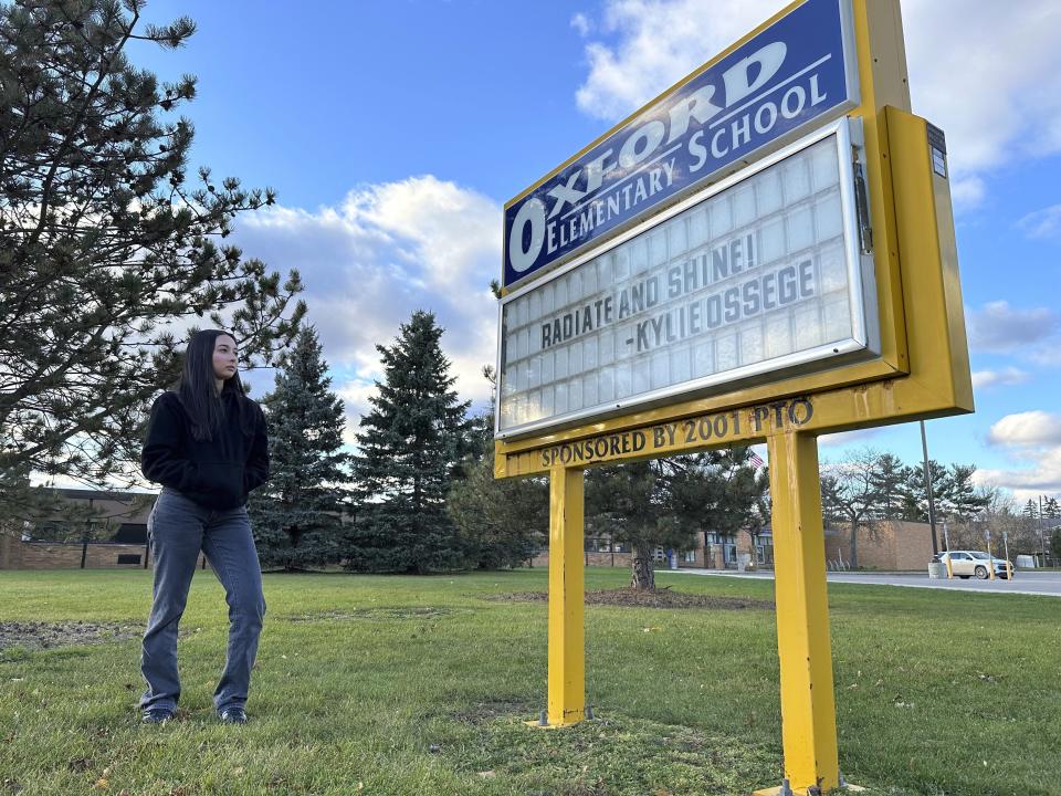 Kylie Ossege stands outside Oxford Elementary School Saturday, Nov. 11, 2021, in Oxford Township, Mich. The sign outside the school features a phrase – "radiate and shine" – that Ossege used as part of her commencement address at Oxford High School in 2022. Ossege was severely injured in a 2021 mass shooting at the high school. (AP Photo/Mike Householder)