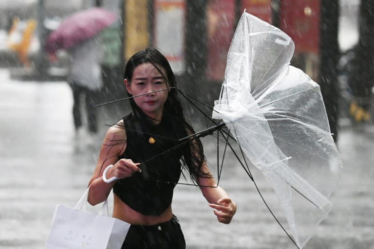 Una joven sostiene un paraguas roto por el viento en medio de un fuerte aguacero, el 31 de julio de 2024 en Pekín (Greg Baker)