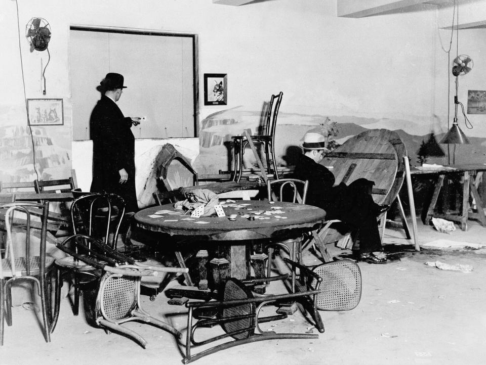 FILE - In this Dec. 31, 1931, file photo the wrecked speakeasy in the Hotel Victoria in mid-Manhattan, where Louis Levine, alias Louis Taylor, a small-time gambler, was killed by one of three gunmen earlier in the day in New York. A bystander points to a bullet hole in the wall, while another is seated in the chair where Levine, known as "Crooked Neck Louie", was gambling when he was shot. (AP Photo, File)