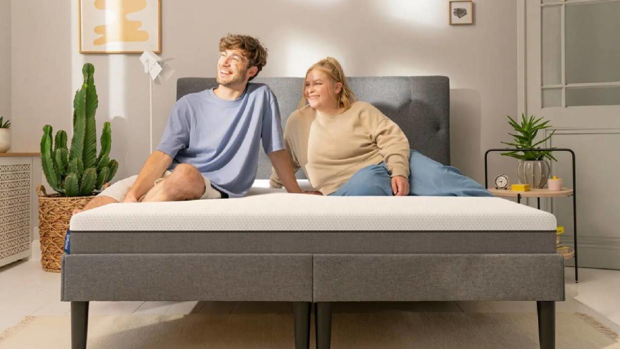  A couple smiling while sitting on an Emma mattress. 
