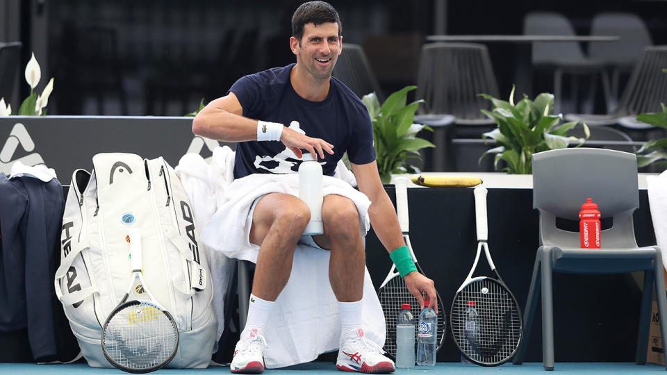 Novak Djokovic smiles and reaches for a drink bottle while taking a break during a practice session in Adelaide.