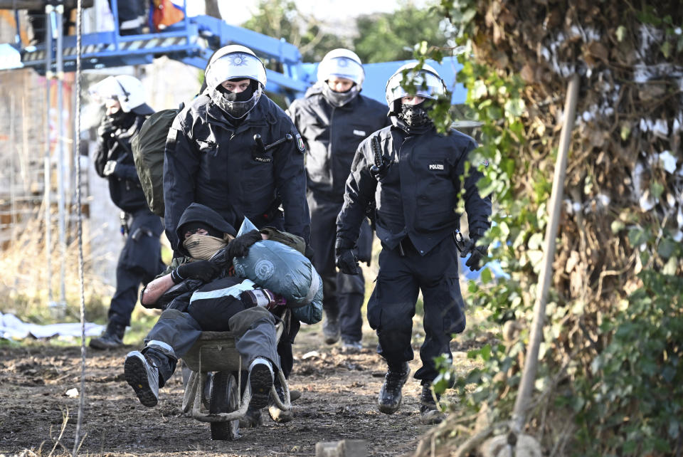 Police officers push a climate activist with a wheelbarrow off the site in the village Luetzerath in Erkelenz, Germany, Sunday, Jan. 15, 2023. The energy company RWE wants to excavate the coal lying under Luetzerath, for this purpose, the hamlet on the territory of the city of Erkelenz at the opencast lignite mine Garzweiler II is to be demolished. (Federico Gambarini/dpa via AP)