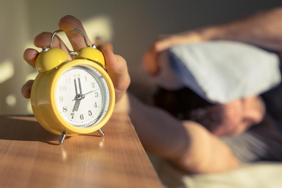 Sleeping man disturbed by alarm clock early in the morning.