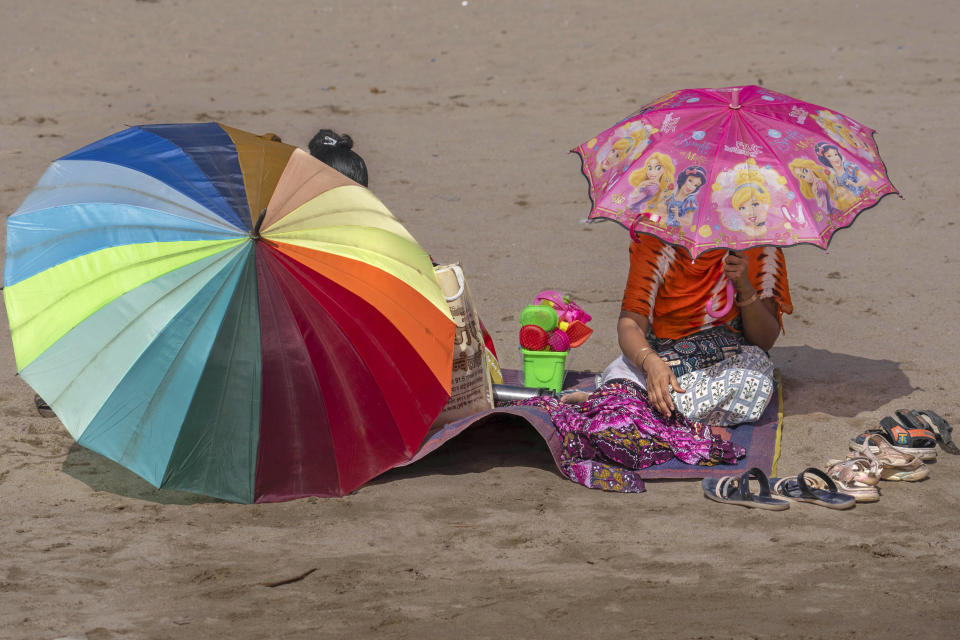 Women sit in Juhu beach holding umbrellas to protect themselves from the sun on a hot summer day in Mumbai, India, Thursday, May 2, 2024. (AP Photo/Rafiq Maqbool)