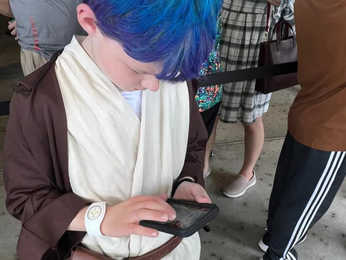 Catie's son (a kid with blue hair in a costume) on a phone on the datapad app