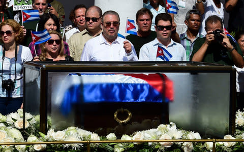 the son of late Cuban leader Fidel Castro, Fidel Castro Diaz-Balart (C), holds a Cuban national flag as he looks at the urn with the ashes of his father - Credit: RONALDO SCHEMIDT /AFP