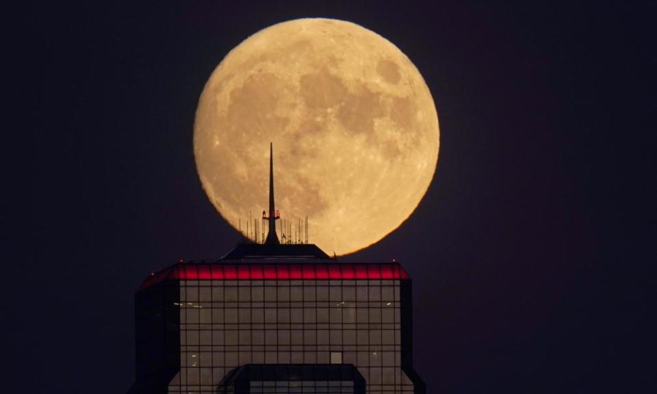 A nearly full moon rises, with an office building in the foreground