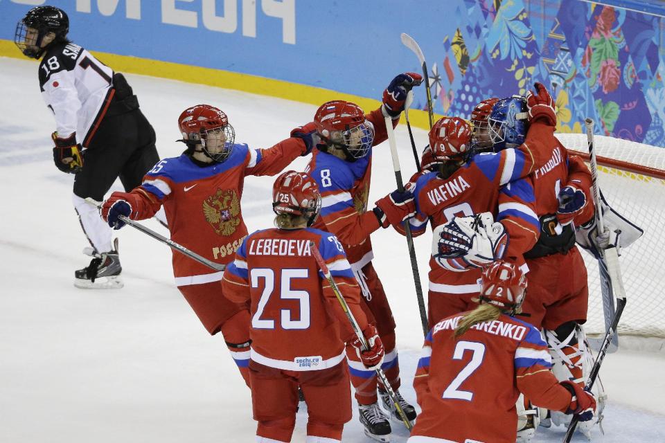Team Russia celebrates their 2-1 win over Japan as Tomoko Sakagami of Japan skates past after the 2014 Winter Olympics women's ice hockey game at Shayba Arena, Tuesday, Feb. 11, 2014, in Sochi, Russia. (AP Photo/Mark Humphrey)