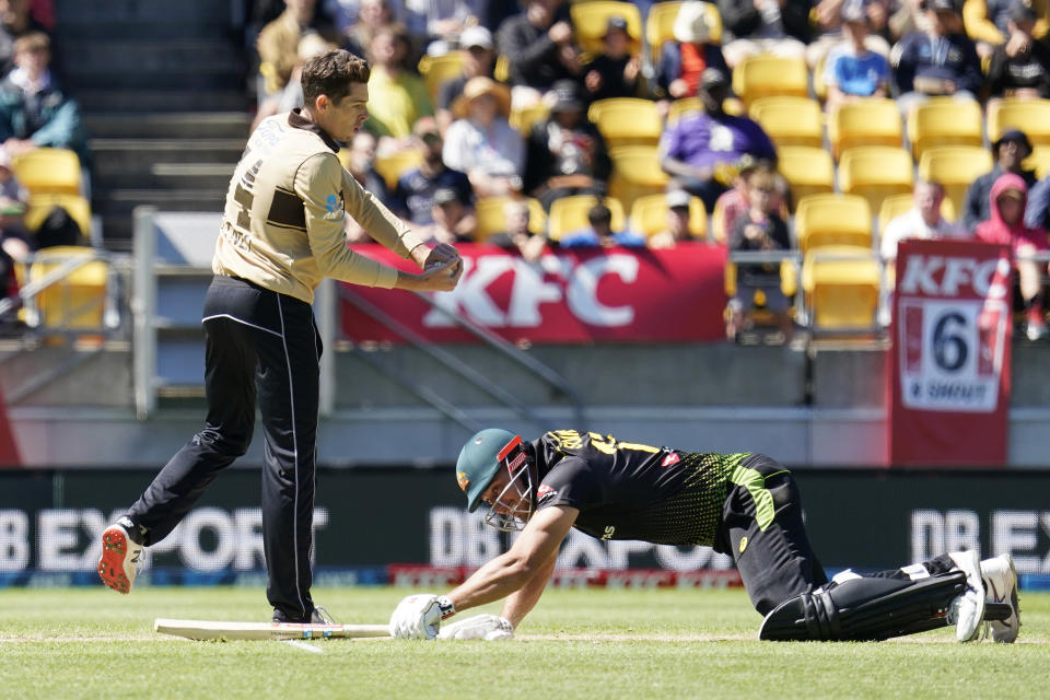 Australia's Marcus Stoinis, right, reaches to make his ground as New Zealand's Mitchell Santner takes the ball during their 5th T20 cricket international match at Wellington Regional Stadium in Wellington, New Zealand, Sunday, March 7 , 2021. (John Cowpland/Photosport via AP)