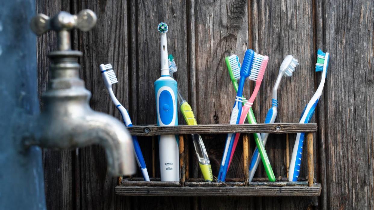  Manual and electric toothbrushes being stored in the bathroom near a tap. 