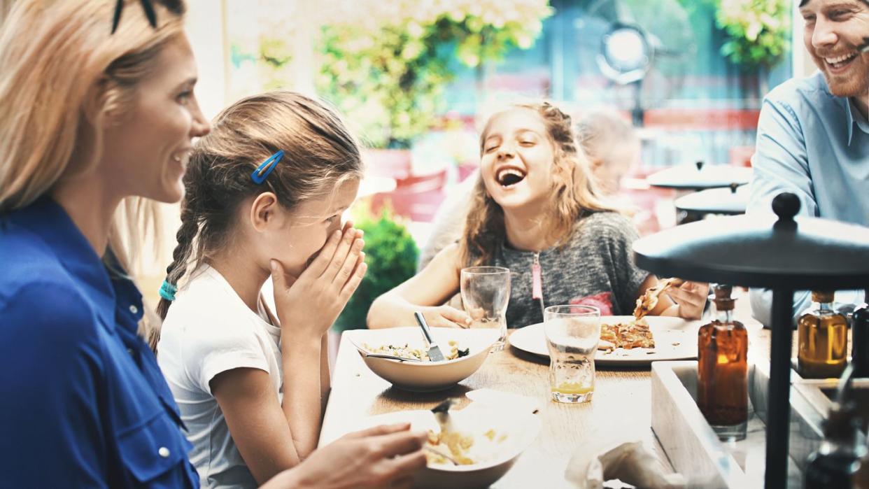 closeup of a mid 30s married couple with their two daughters having lunch at a restaurant the girls are telling jokes and making everybody laugh
