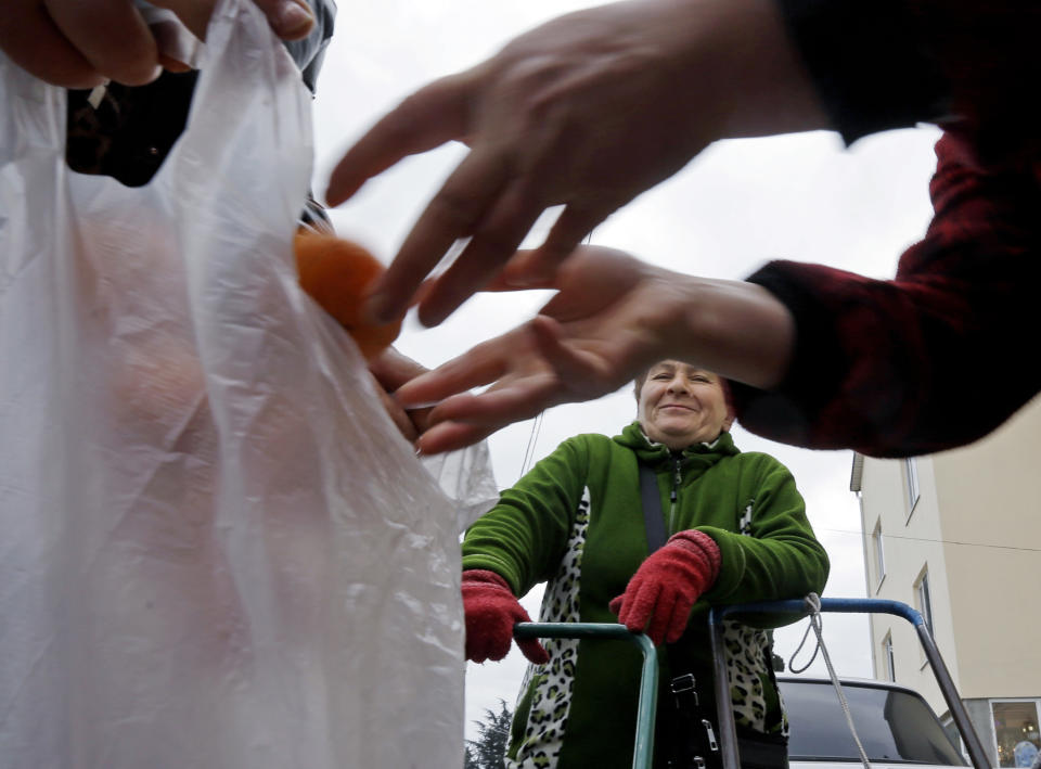 Mukhmunad Ashabokova watches as someone puts tangerines in a bag at the Abkhazian border Wednesday, Feb. 5, 2014, near Sochi, Russia. Most days in the tangerine season, she rolls her squat cart loaded down with the fruit across the bridge over Psou River from her garden about two miles inside Abkhazia. (AP Photo/Morry Gash)